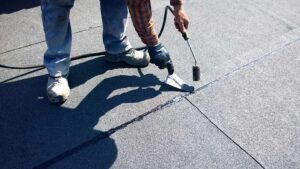 Homeowner inspecting curled shingles and roof flashing from a ladder beside a residential house.