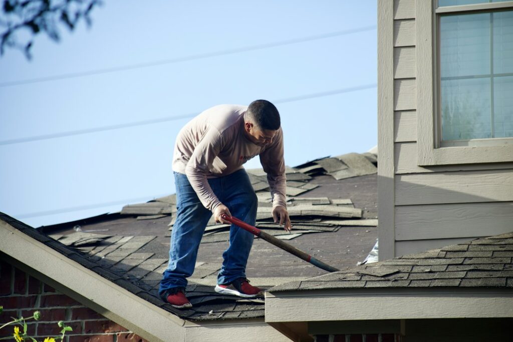 Homeowner reviewing roof damage photos and insurance documents beside a window while storm clouds gather outside.